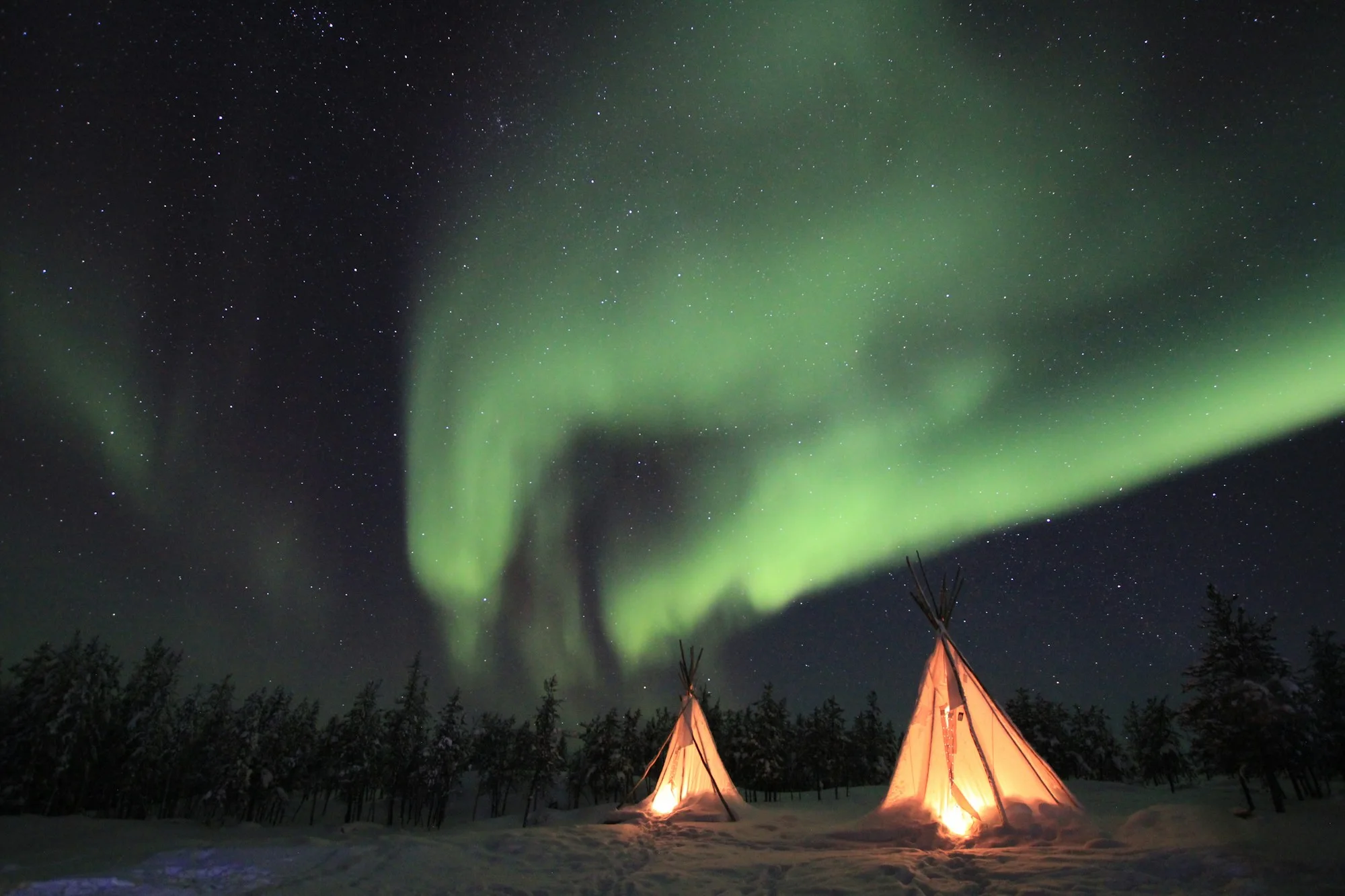 Tents glowing under the northern lights on a group trip